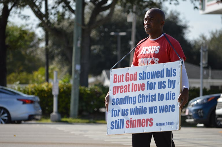 Man holding a sign with a Christian message on a busy urban street.