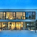 Modern house at dusk with floor-to-ceiling windows, every room lit and visible from outside